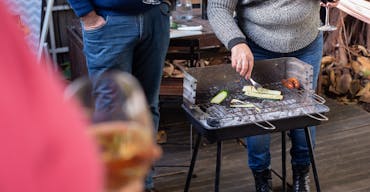 A casual outdoor BBQ in Portugal with friends enjoying wine while grilling vegetables and sausages.