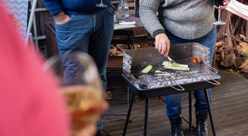 A casual outdoor BBQ in Portugal with friends enjoying wine while grilling vegetables and sausages.