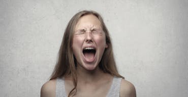 Young woman screaming with emotion, showing braces, against a gray backdrop.