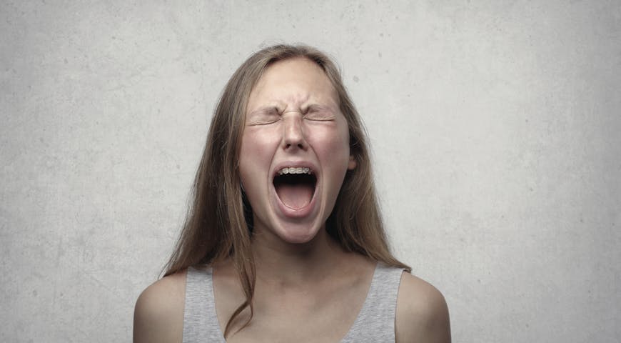 Young woman screaming with emotion, showing braces, against a gray backdrop.